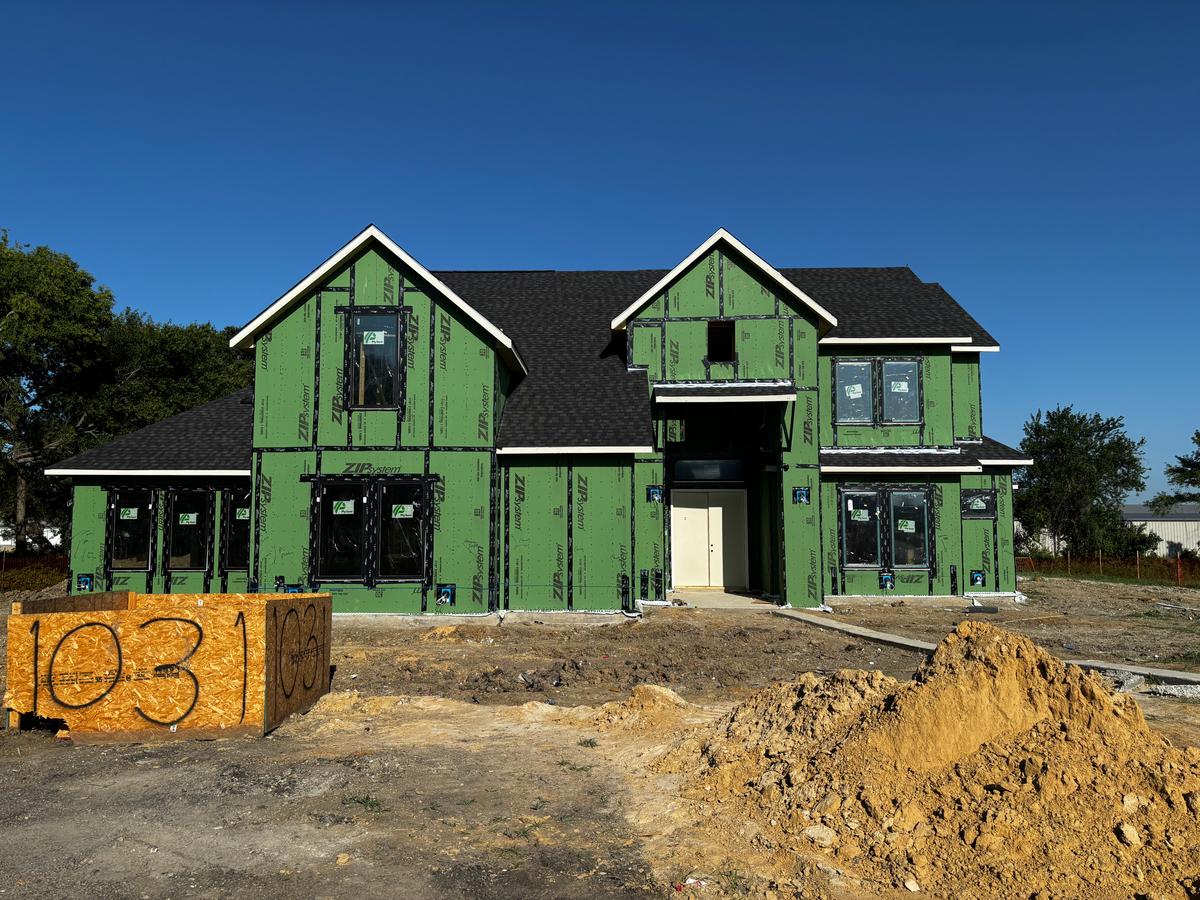 A new-construction home wrapped in green house wrap on a freshly graded lot in Celina, TX.